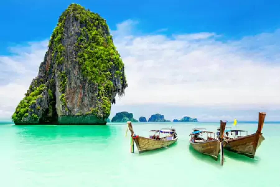 Traditional longtail boats by a lush cliff on a turquoise sea.