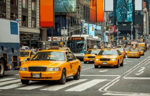 A bustling New York City street filled with yellow taxis navigating through traffic under a clear blue sky.