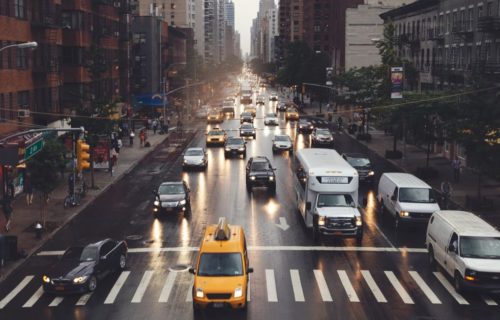 A bustling city street filled with cars, taxis, and buses navigating through the urban landscape.