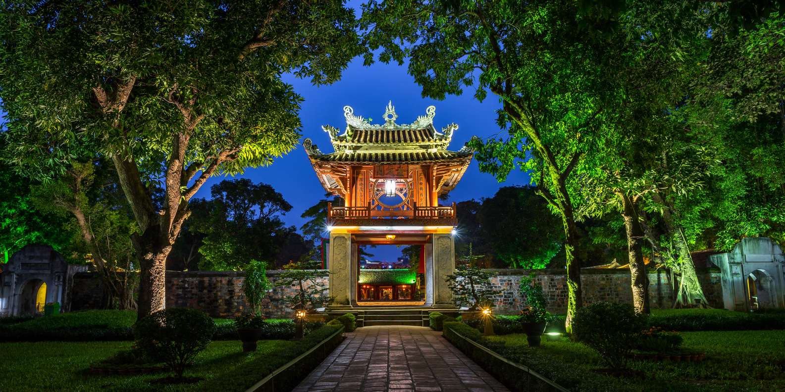 A dark garden gate illuminated by soft moonlight, surrounded by shadowy plants and trees, creating a serene nighttime atmosphere.