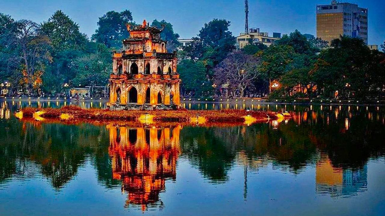Scenic view of Hoan Kiem Lake in Hanoi, Vietnam, featuring lush greenery and traditional architecture along the shoreline.